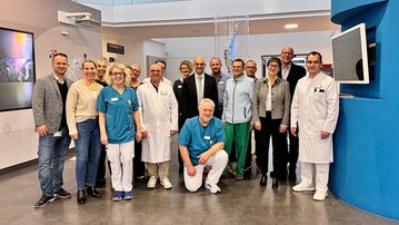 Gruppe von medizinischem Personal und Fachleuten in einem modernen Krankenhausumfeld, alle in Arbeitskleidung, posierend für ein Gruppenfoto.