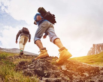 Zwei Wanderer steigen einen felsigen Hang hinauf, ausgestattet mit Rucksäcken und Wanderschuhen, umgeben von einer malerischen Landschaft.