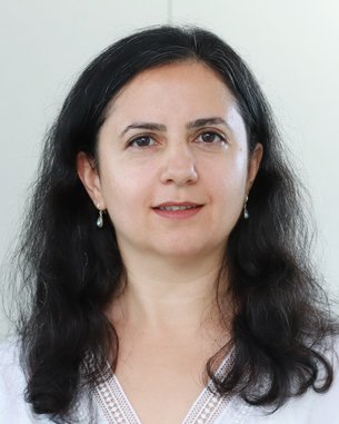 Eine Frau mit langen, lockigen, dunklen Haaren und Ohrringen, die in die Kamera schaut. Sie trägt ein helles Oberteil.