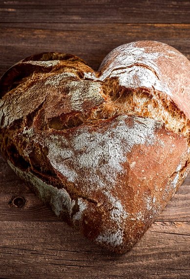 Herzförmiges Brot auf einer Holzoberfläche, mit einer rustikalen Kruste und einer leicht unregelmäßigen Form.