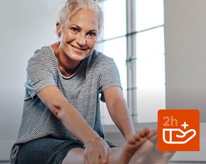 Eine ältere Frau sitzt auf einer Yogamatte und dehnt sich, während sie lächelt. Ein Symbol zeigt eine Zeitangabe von über 2 Stunden.