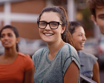 Eine Gruppe junger Menschen steht zusammen, während eine Frau mit Brille lächelt und in die Kamera schaut.