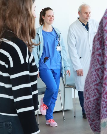 Eine Krankenschwester in blauer Arbeitskleidung steht mit einem Lächeln, während ein Arzt in einem weißen Kittel neben ihr steht.