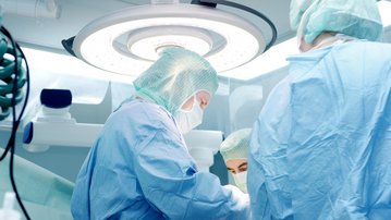 Chirurgisches Team in blauer Schutzkleidung bei einer Operation unter einem hellen OP-Licht.