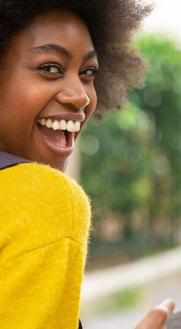 Junge Frau mit Kopfhörern und buntem Pullover, die auf ihr Smartphone schaut, während sie auf einer Straße steht.