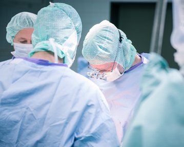 Chirurgisches Team in OP-Kleidung führt einen Eingriff durch, konzentriert auf den Patienten.