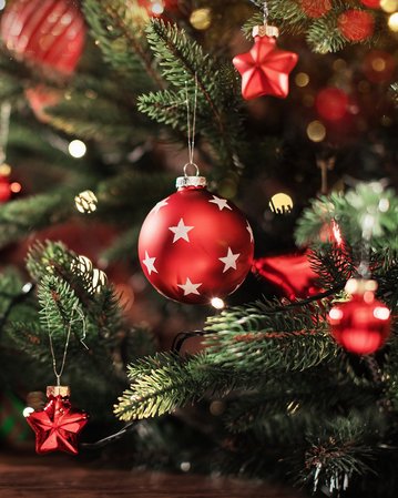 Ein geschmückter Weihnachtsbaum mit roten Kugeln und Sternen, umgeben von verschwommenen Lichtern und Geschenken im Hintergrund.