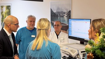 Eine Gruppe von Fachleuten in einem medizinischen Umfeld diskutiert vor einem Computerbildschirm, während sie sich auf die Datenanalyse konzentrieren.