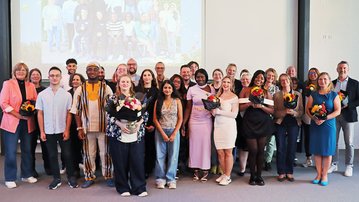 Gruppenfoto von Teilnehmern einer Veranstaltung, die Blumensträuße halten. Im Hintergrund ist eine Präsentation zu sehen.