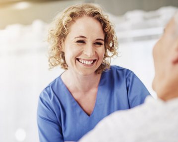 Eine Krankenschwester lächelt und spricht mit einem Patienten im Krankenhausbett, während sie ihm Aufmerksamkeit und Pflege bietet.