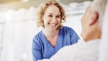 Eine Krankenschwester lächelt und spricht mit einem Patienten im Krankenhausbett, während sie ihm Aufmerksamkeit und Unterstützung bietet.