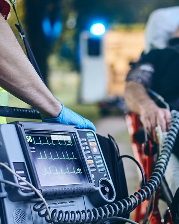 Ein Rettungssanitäter bedient ein medizinisches Gerät zur Überwachung von Vitalzeichen, während ein Patient auf einer Trage liegt.