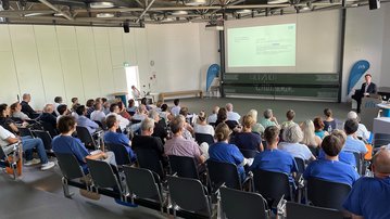 Eine Gruppe von Menschen sitzt in einem Seminarraum, während ein Referent eine Präsentation auf einer Leinwand zeigt.