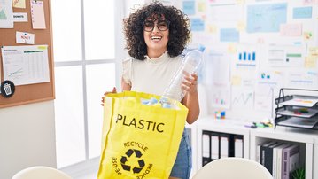 Eine Person mit lockigem Haar hält eine gelbe Tasche mit der Aufschrift "PLASTIC" und einer Wasserflasche, bereit zum Recycling.