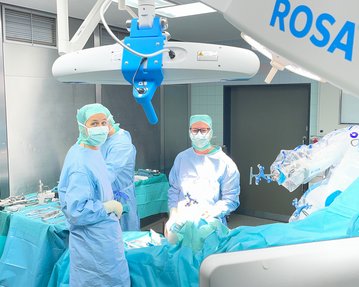 Chirurgisches Team in blauer Kleidung und Masken, umgeben von medizinischen Instrumenten und einem Operationsroboter im Operationssaal.